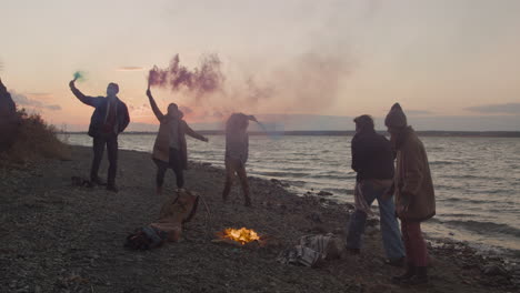 groupe d'amis adolescents courant autour d'un feu de joie tenant des cierges colorés au bord de la mer