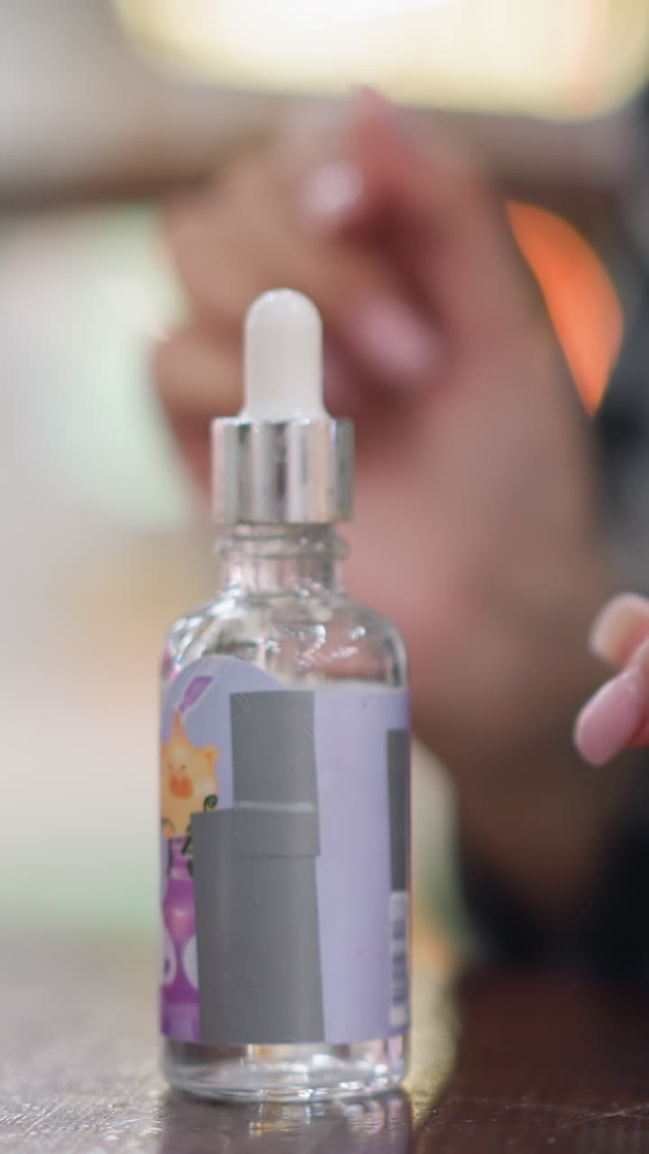 Primo piano di mani con un flacone contagocce che mostra un rituale con siero caldo in casa, unghie curate che svitano delicatamente il tappo argentato, la pipetta si riempie di liquido trasparente, gocce lente e precise che cadono in un flacone di vetro su un tavolo di legno