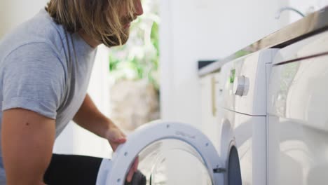 Caucasian-man-putting-apron-in-the-washing-machine-at-home