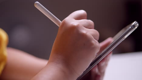 close-up of an individual scribbling and writing some notes using a portable electronic tablet and a stylus pen