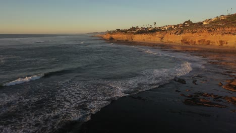 stunning drone shot follows the rugged cliffs during sunset, with the waves crashing below and the sun casting a warm, golden glow over the dramatic coastline