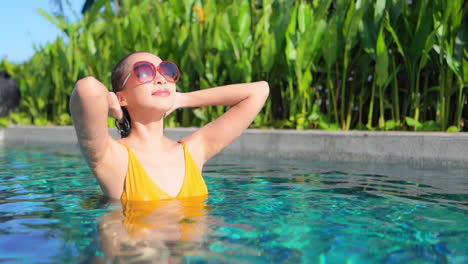 sexy exotic woman in tropical swimming pool caresses her wet hair on sunny day, close up full frame slow motion