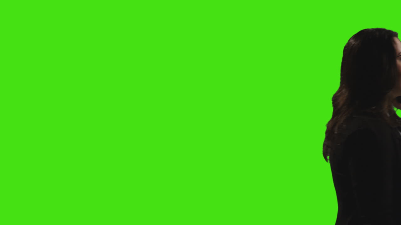 vista laterale di una donna d'affari che parla al cellulare che cammina attraverso la cornice contro lo schermo verde