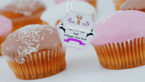 animation of christmas greetings on tag over cupcakes on white background