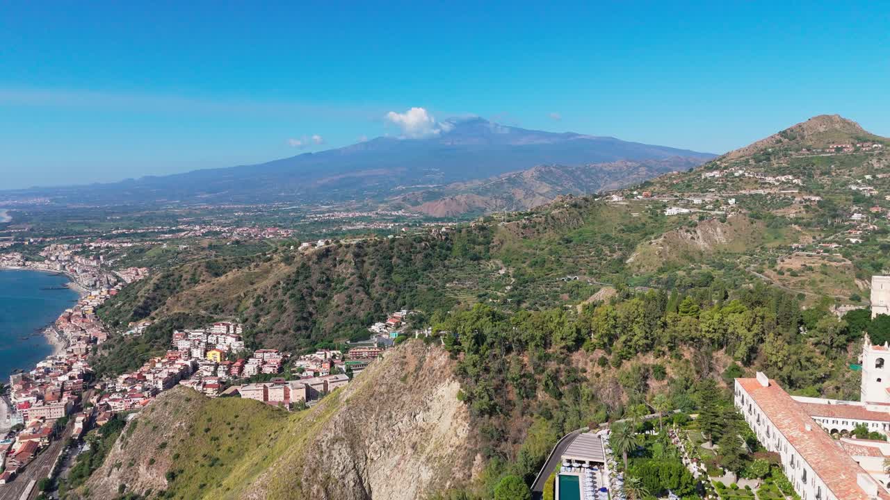 Aerial pull-away shot from Mount Etna, revealing the towns of Taormina and Naxos with the Sicilian coastline stretching into the distance