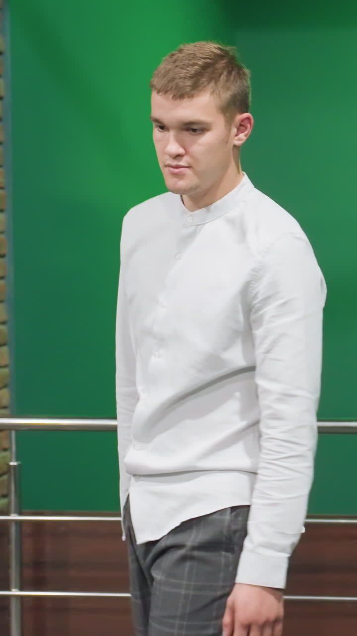 색 셔츠와 체커 바지를 입은 남성이 레일을 들고 계단을 올라가며 초록색 조명 아래 집중된 표현, 현대적인 금속 레일링과 녹색 벽으로 세련된 실내 설정