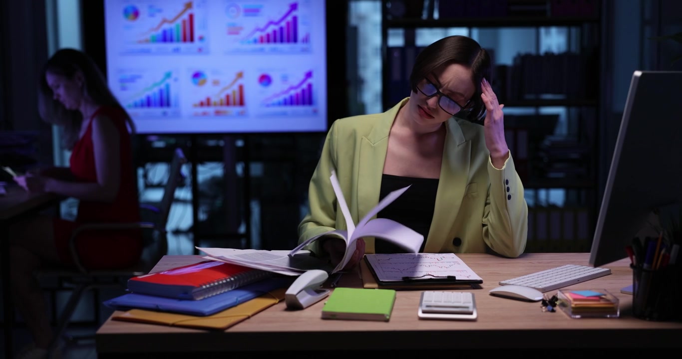 Young businesswoman checks reports as sits at desk in dark office