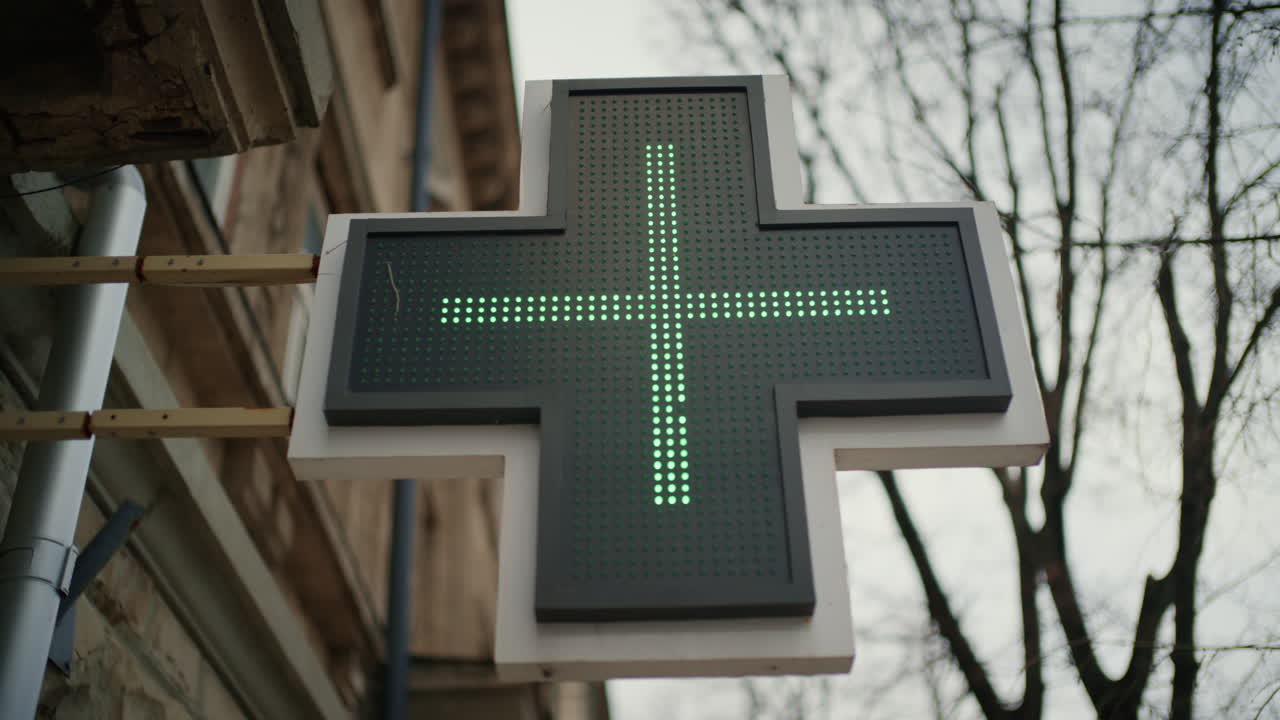Illuminated green pharmacy cross sign outside a building