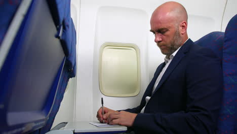 low angle of a man with a beard and suit filling out an immigration form paper on an airliner plane