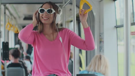 close-up portrait of a young woman with headphones standing in the modern tram. a woman in glasses listens to music in a tram.