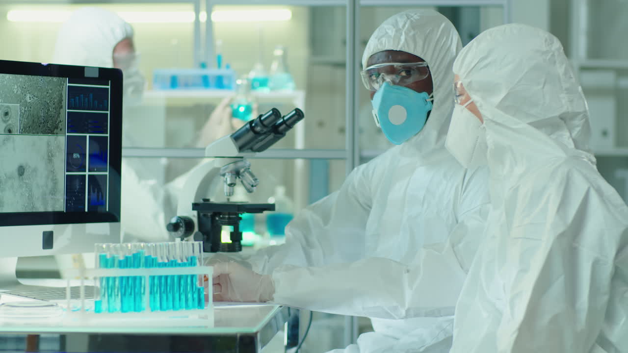Multiethnic Scientists in Coveralls Discussing Micrograph on Computer