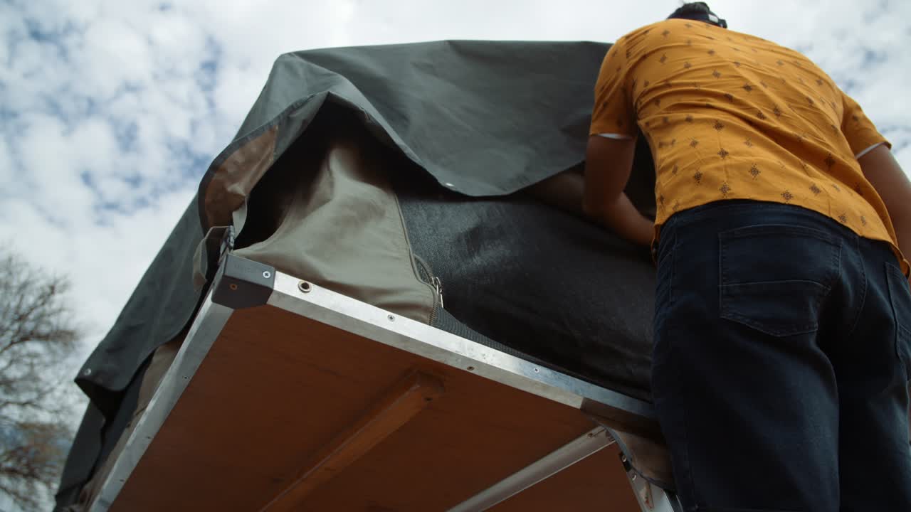 Hand held shot of a Tourist Caucasian white male in Africa as he climbs up a ladder to zip down his rooftop canvas tent