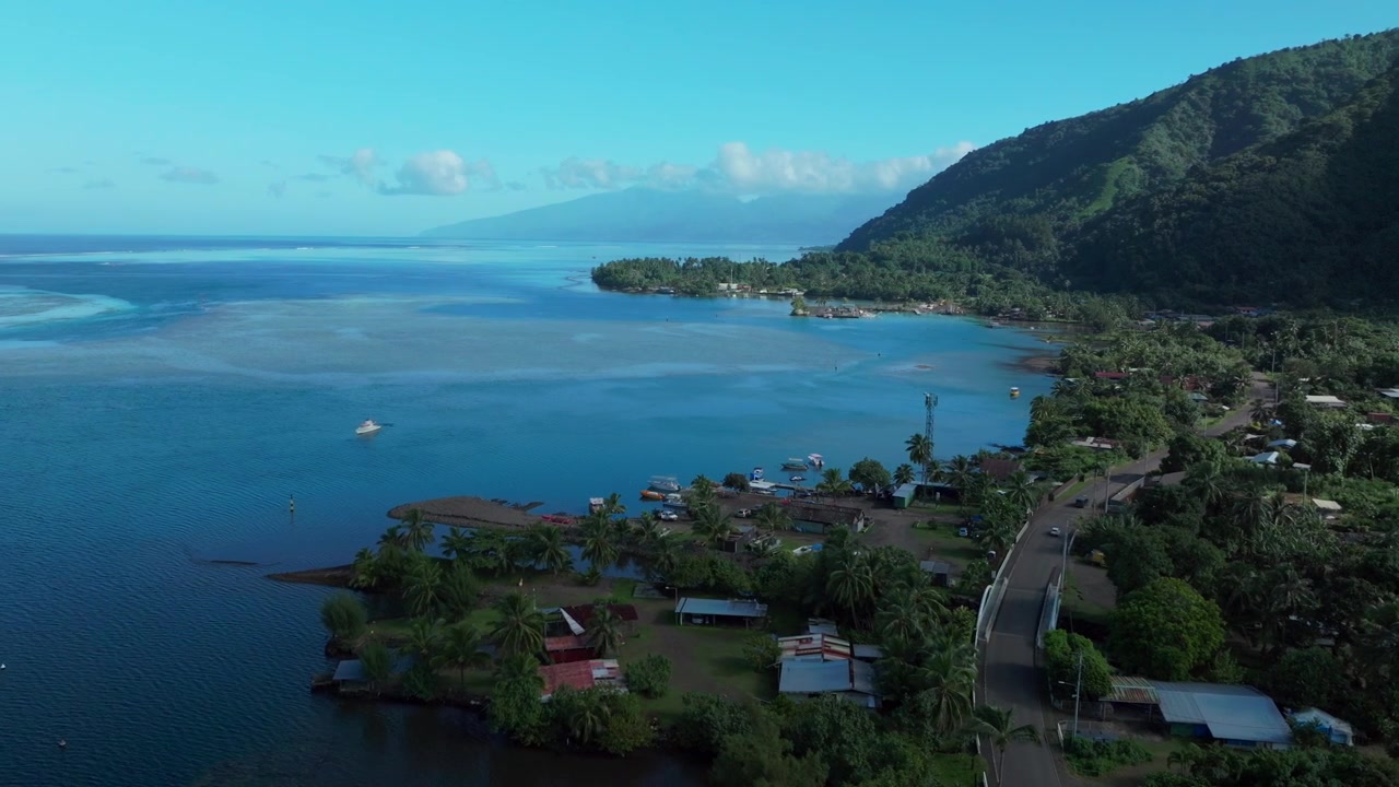 Teahupoo, Tahiti, Polinesia Francese: vista aerea con drone. Furgone sulla strada costiera dell'isola verso Papeete in una mattina soleggiata. Baia, canale, barriera corallina e fianco della montagna. Traffico di auto e jeep in viaggio su strada, con una curva a sinistra.