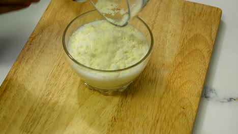 close up of person hand pouring milk powder into a bowl of milk.