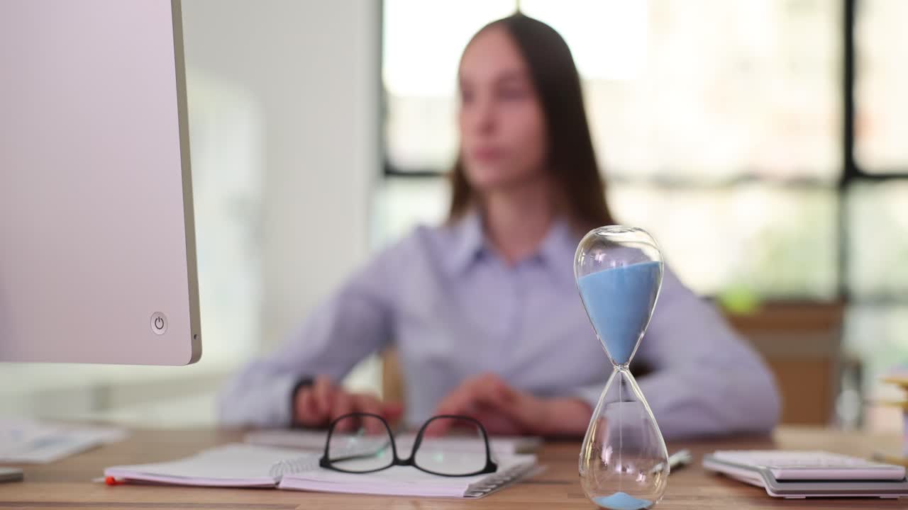 Woman working at desk with hourglass