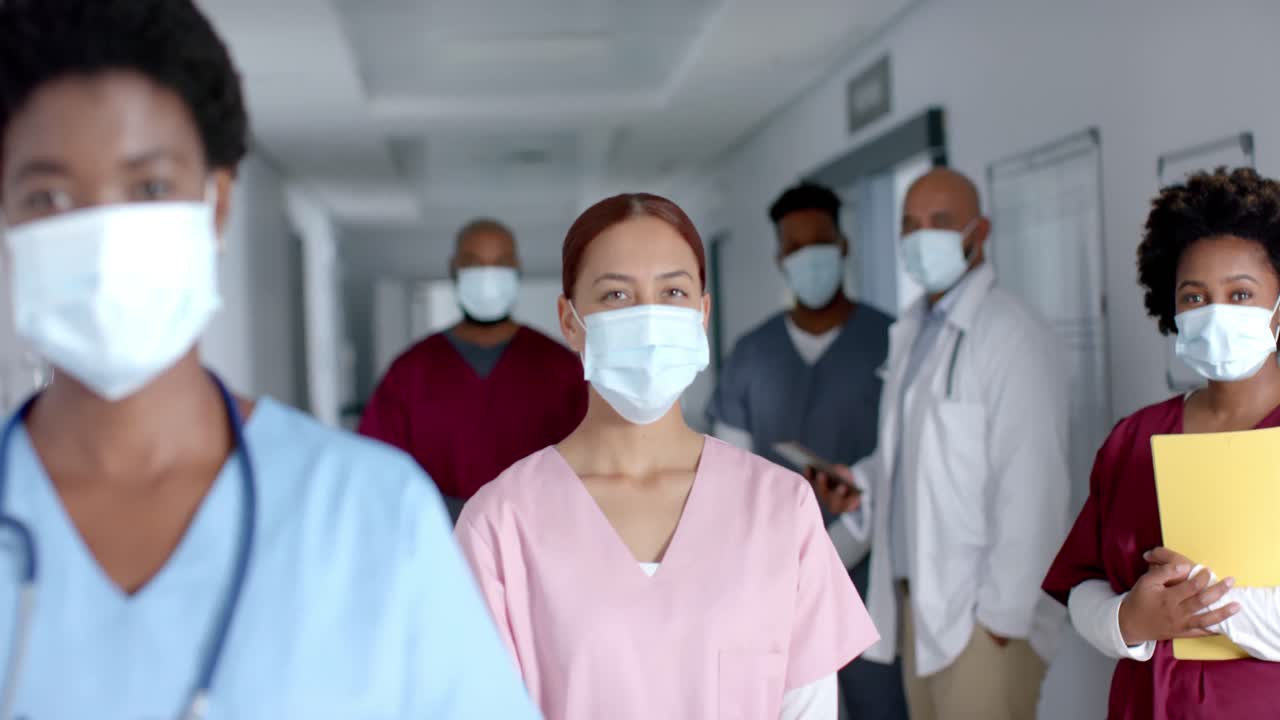 Ritratto di medici felici di diverse etnie che indossano mascherine in corridoio, al rallentatore