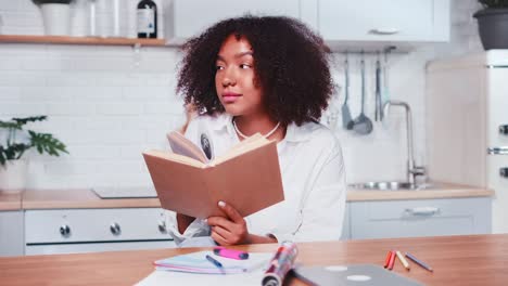 smiling african american woman reads book and dreams in cozy white kitchen