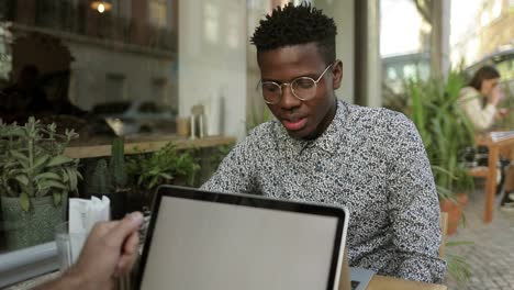 Young-man-using-laptop-and-talking-with-someone-on-foreground