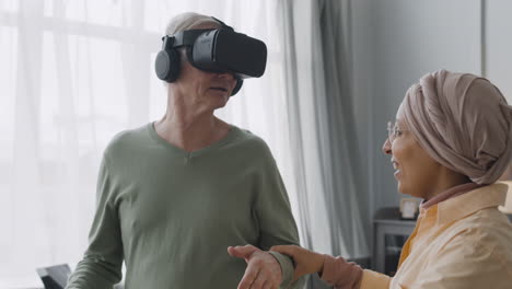 mujer árabe de mediana edad ayudando a un anciano feliz a usar gafas de realidad virtual en casa