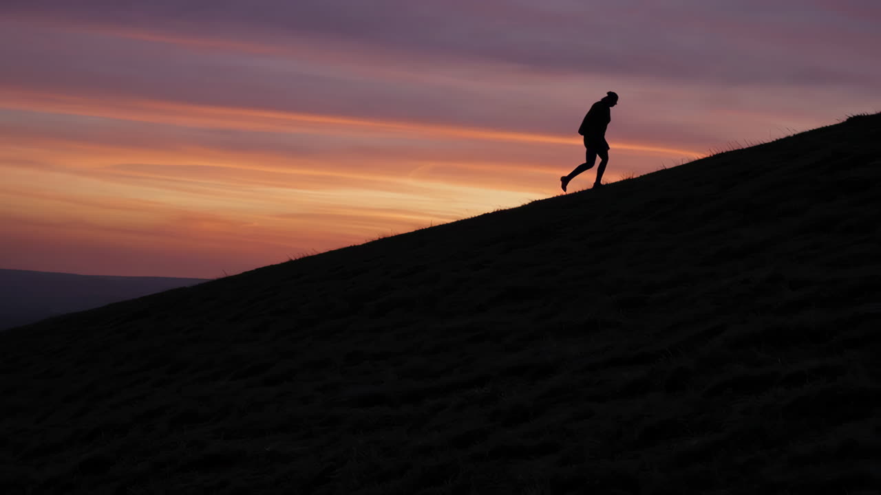 Silhouette of Person Walking Up a Sand Dune at Sunset