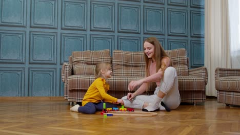 a young girl plays with a wooden toy train while sitting on the floor with her older sister.