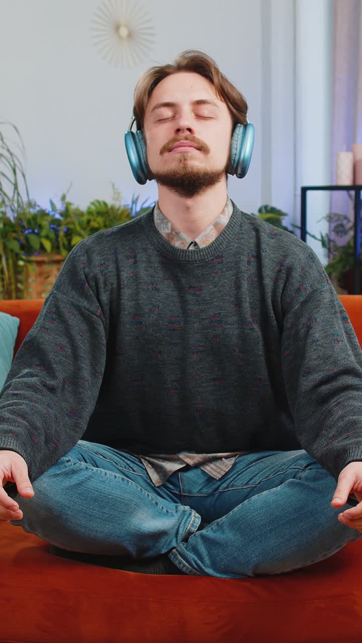 Bearded man listening music breathes deeply meditating with concentrated thoughts peaceful at home