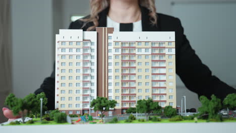 close up of professional woman dressed in black carrying detailed building model toward office desk, showcasing modern real estate concept and architectural miniature with urban layouts