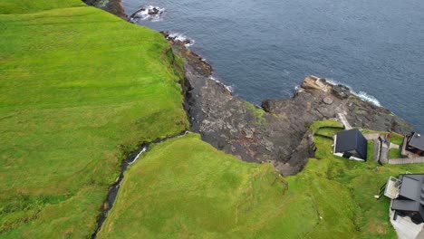 Drone-pullback-tilt-up-reveals-quaint-village-of-Mikladalur-from-its-waterfall-on-Kalsoy,-Faroe-Islands