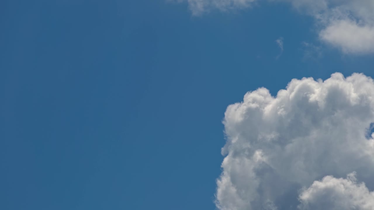 Fluffy clouds move slowly across a bright blue sky in daylight