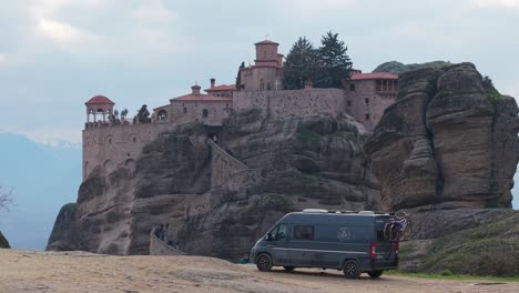 scenic drone shot of a campervan parked on a hill at meteora, greece. a majestic monastery is revealed in the background, blending travel freedom with ancient heritage in an autumn landscape
