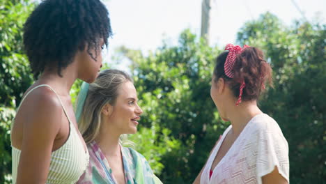 three diverse female friends chatting and laughing together outdoors by pool