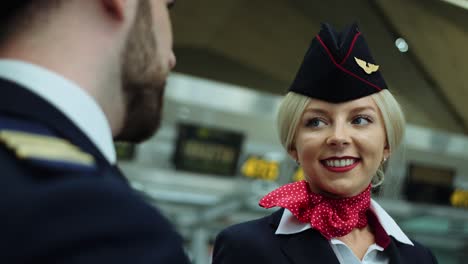in airport stewardess with blond hair smiling affably, talking with pilot. european woman dressed in dark blue uniform, scarlet red scarf tied on her white shirt. cinematic shot on red camera. 2 models.