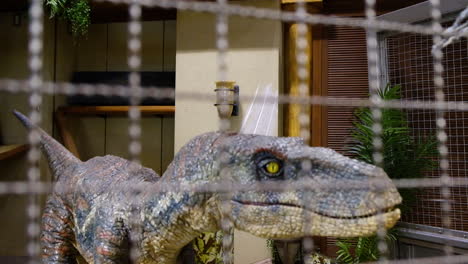 a robotic velociraptor dinosaur roaring inside a cage robot