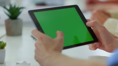 manos masculinas tocando la tableta de pantalla verde en el interior. brazos del hombre usando un dispositivo digital.