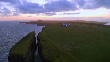 beautiful aerial shot of loop head lighthouse, the sea stack, and an "éire" sign against a warm twilight sky