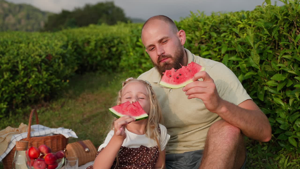 Padre e hija disfrutando de un picnic con sandía en una plantación de té