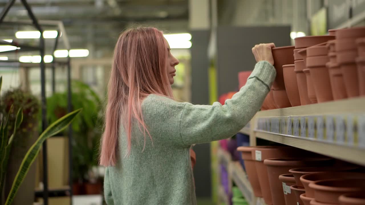 mujer comprando macetas de arcilla para plantas caseras de los estantes de una floristería