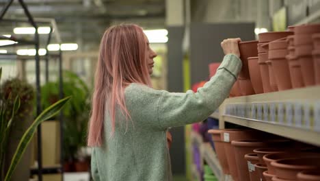 woman buying clay pot for home plants from shelves of a flower shop