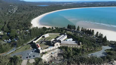 cinematic aerial view of a historic gaol surrounded by scenic coastline and mountain backdrop