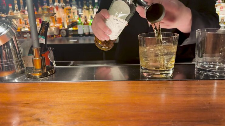 Un barista professionista versa un liquido ambrato da una bottiglia in un bicchiere in un bar.