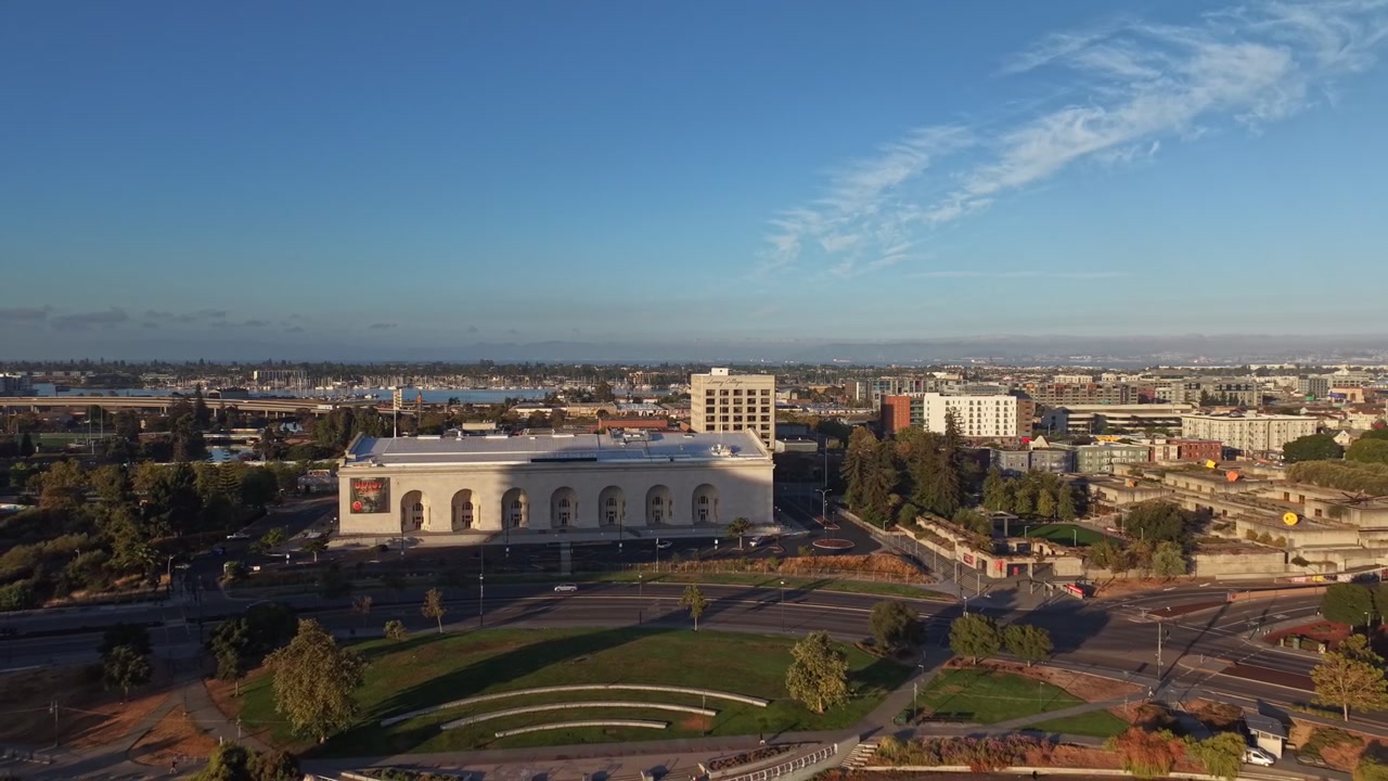 Dronevideo viser frem Henry J. Kaiser Center for the Arts og Oakland Museum i gyllent morgenlys, med Lake Merritt-hagene, buet arkitektur og klar bysilhuett sett ovenfra