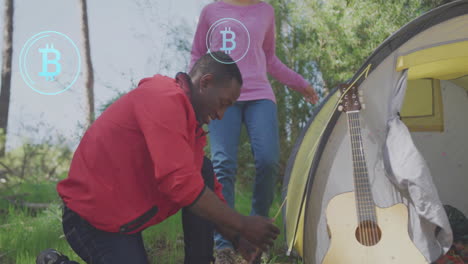 man setting up tent with bitcoin symbol animation over guitar nearby