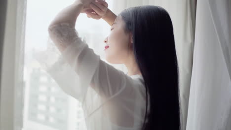 real shot of beautiful girl getting up in white pajamas waking up in her bed sitting near the big window fully rested and open the curtains stretching in the morning to get fresh air and sunshine