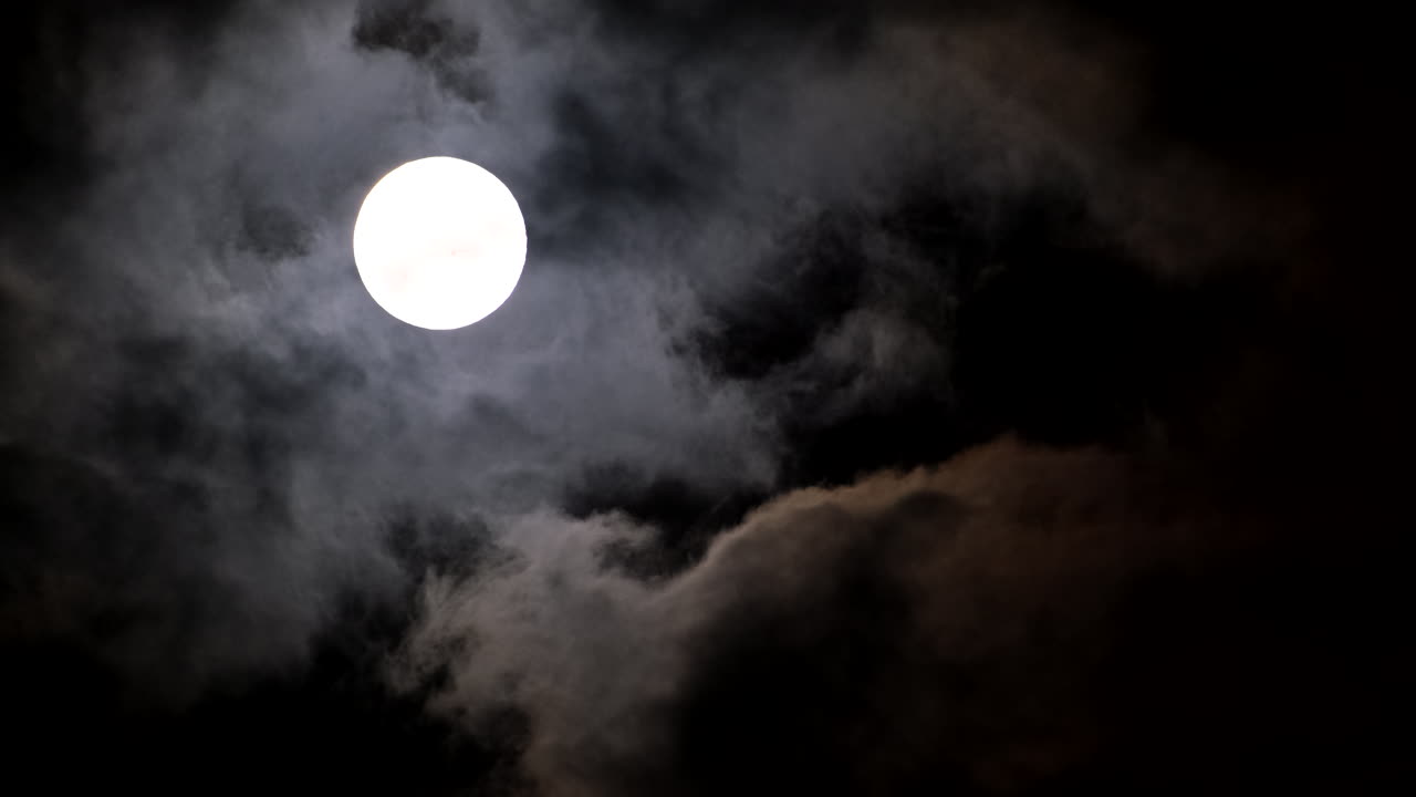 Ominous scene with full moon in dark night sky and dark passing clouds