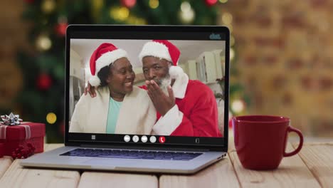 Pareja-De-Ancianos-Afroamericanos-Con-Sombreros-De-Santa-En-Videollamada-En-Una-Computadora-Portátil,-Con-árbol-De-Navidad