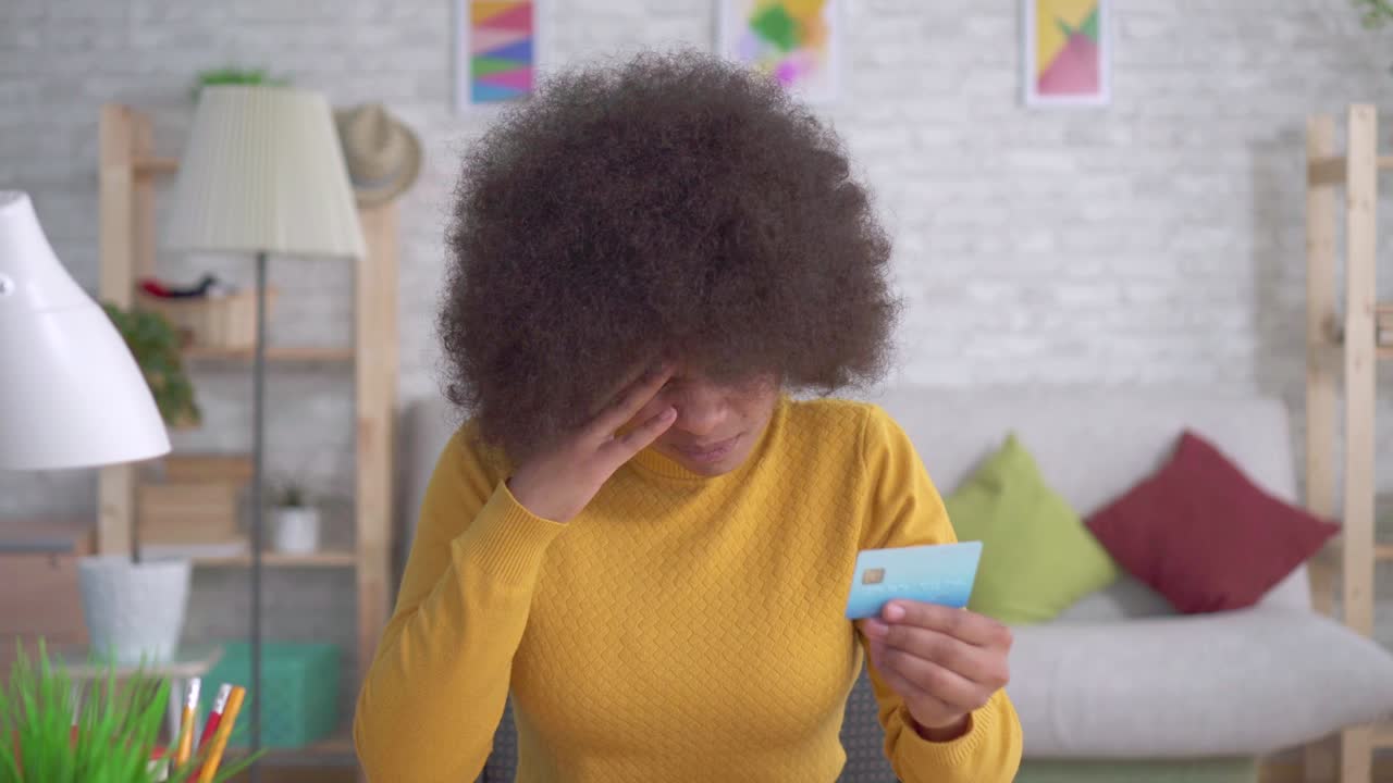 portrait african american woman with an afro hairstyle tired and stressed looking at the Bank card in his hands and crying
