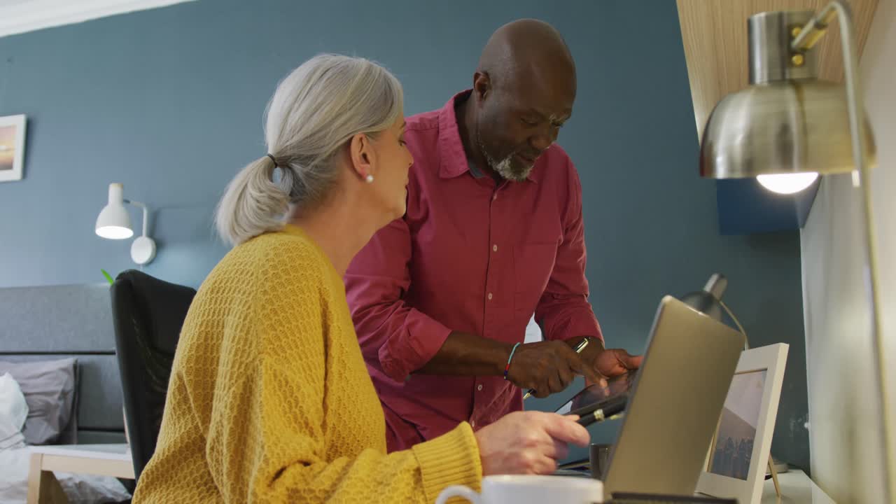 Happy senior diverse couple sitting at table and working