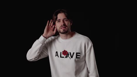 trendy young man listening with hand, deaf gesture, wide, black background