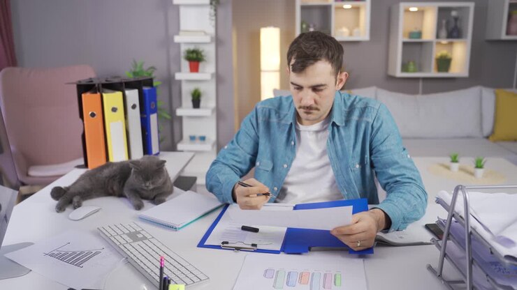 кошка наблюдает за человеком, работающим в его домашнем офисе.