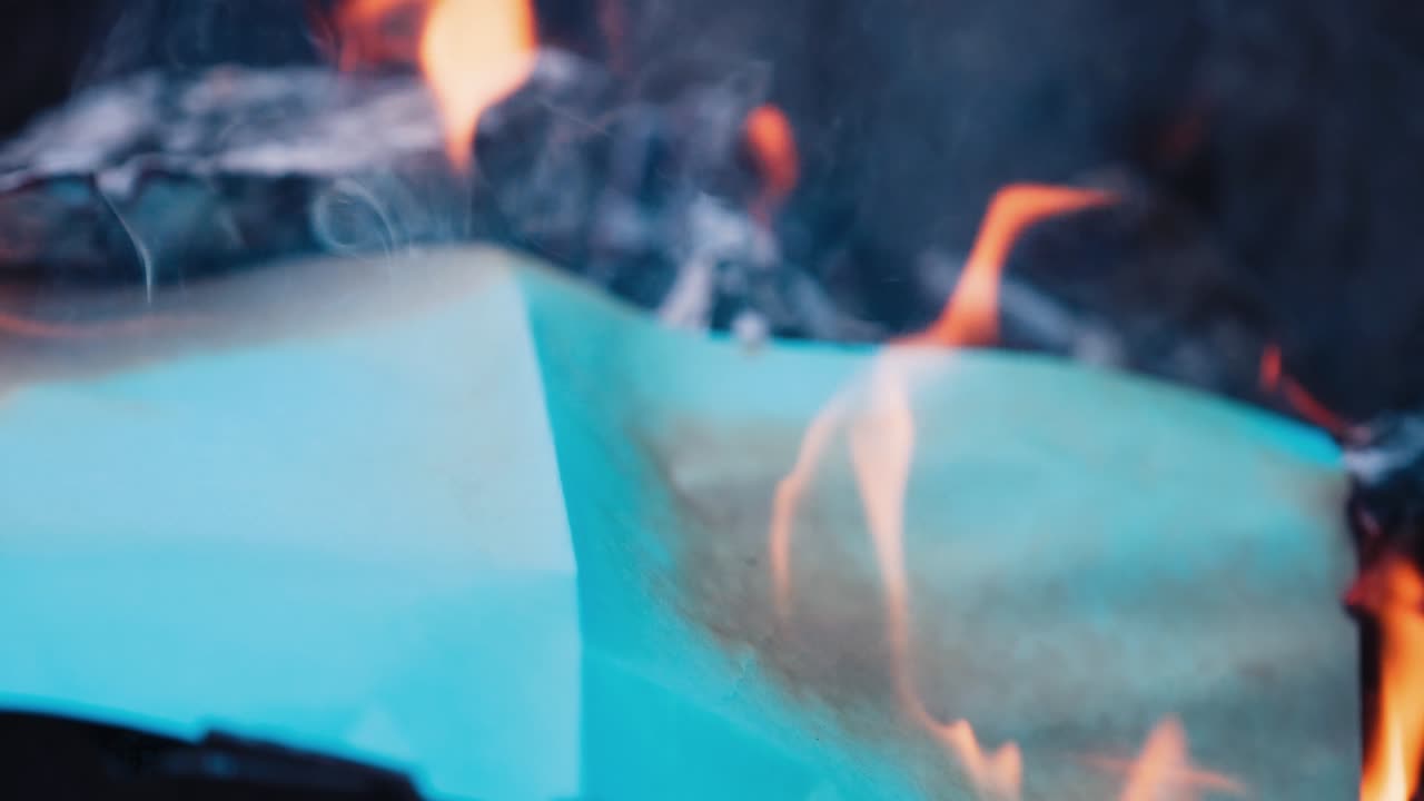 Detailed video of paper burning. Bright fire flame on smoldered logs. White paper becomes black in bonfire. Slow motion. Close-up.
